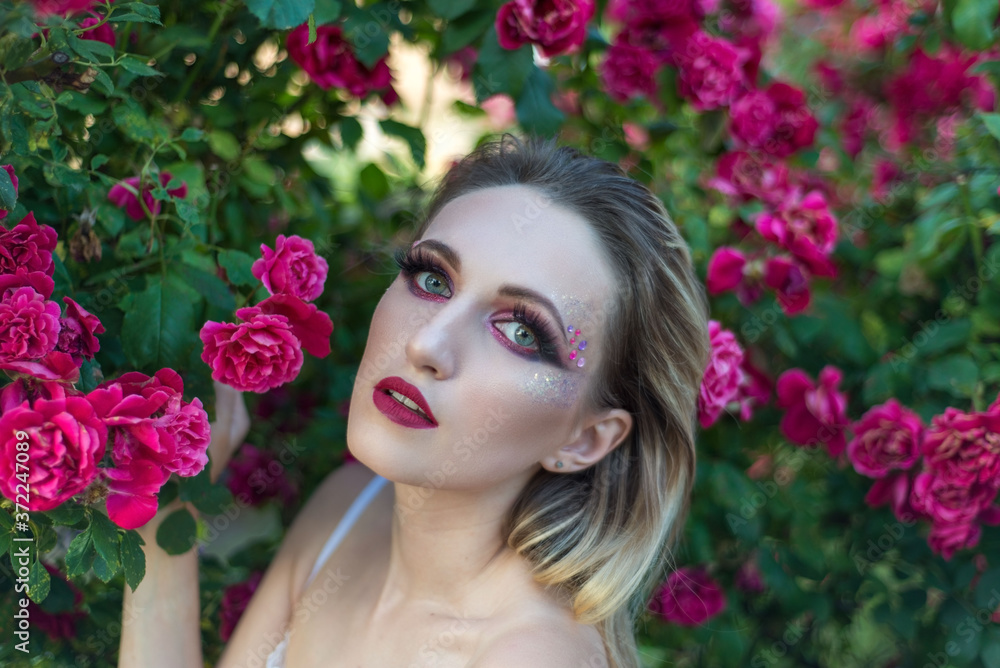 beauty portrait of a young girl of twenty eight years old, on a pink floral background, with false eyelashes. beauty, beautiful feminine portrait of a girl in roses, in creative tinting. evening dress beauty portrait of a young girl of twenty eight years old, on a pink floral background, with false eyelashes. beauty, beautiful feminine portrait of a girl in roses, in creative tinting. evening dress