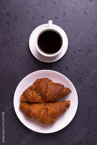 a white ceramic cup of black roasted coffee espresso and a french croissant on the wooden surface
