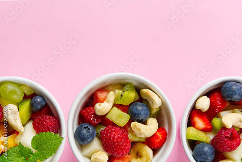 Bowl of healthy fresh fruit salad on pink background  top view copy space.
