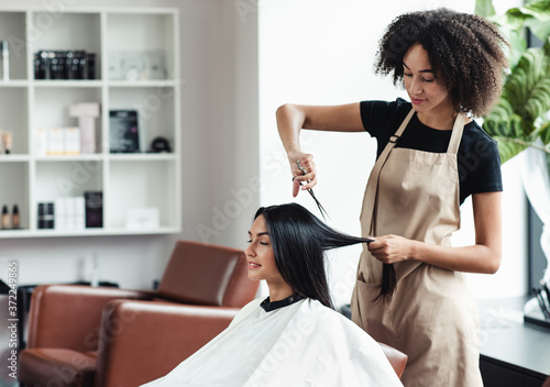 Photographie Young black hairdresser cutting hair of female customer at salon