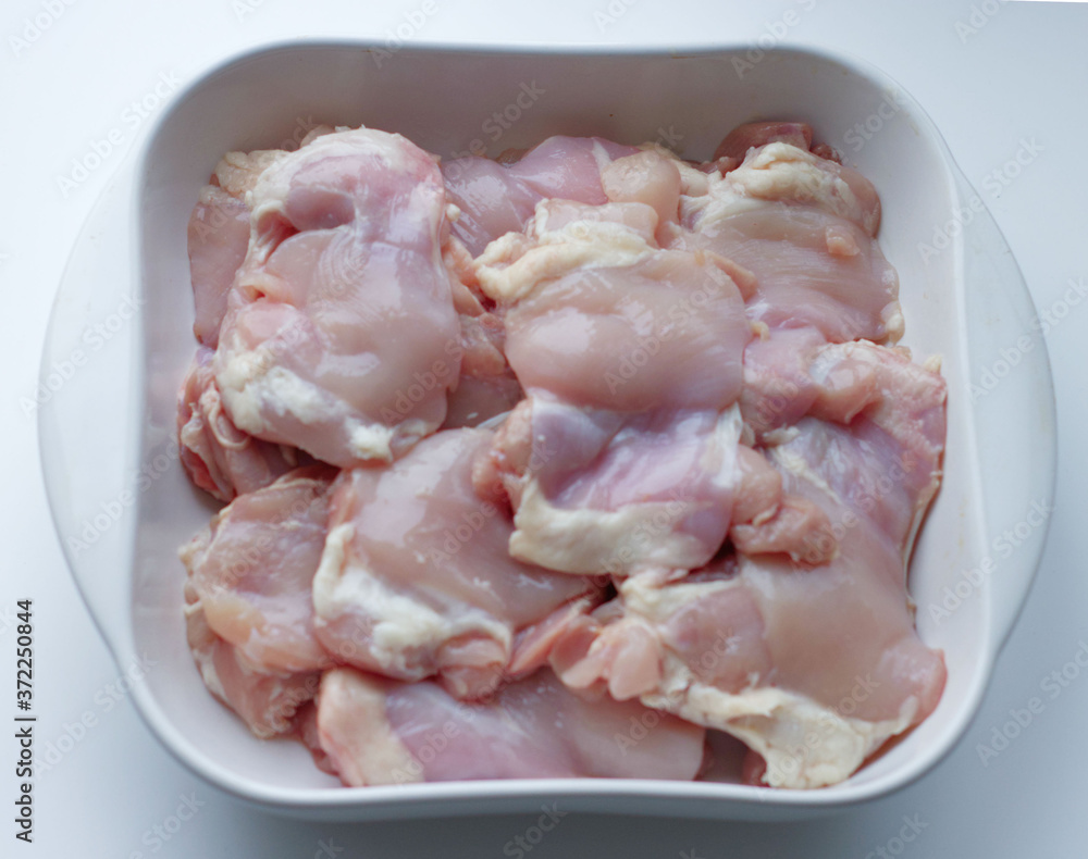 Chicken thigh fillet with skin, in a white glass plate, on a gray background. Ingredients, fresh, cut meat for cooking. Chicken parts, protein. Diet meat, fillet in a plate Chicken thigh fillet with skin, in a white glass plate, on a gray background. Ingredients, fresh, cut meat for cooking. Chicken parts, protein. Diet meat, fillet in a plate