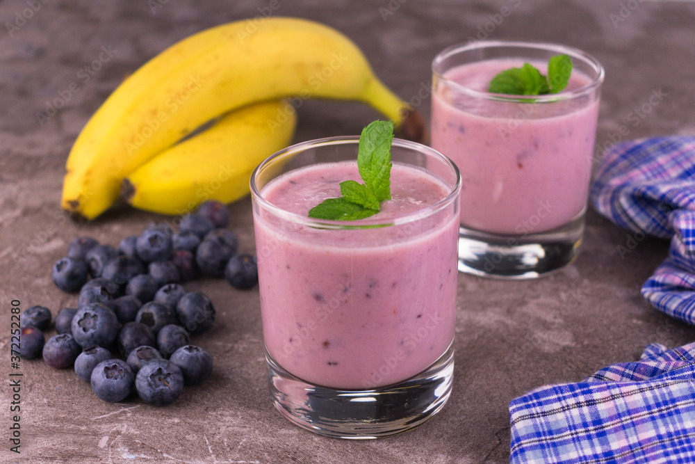 Blueberry banana smoothie in a transparent glass on a gray background. Blueberry banana smoothie in a transparent glass on a gray background.
