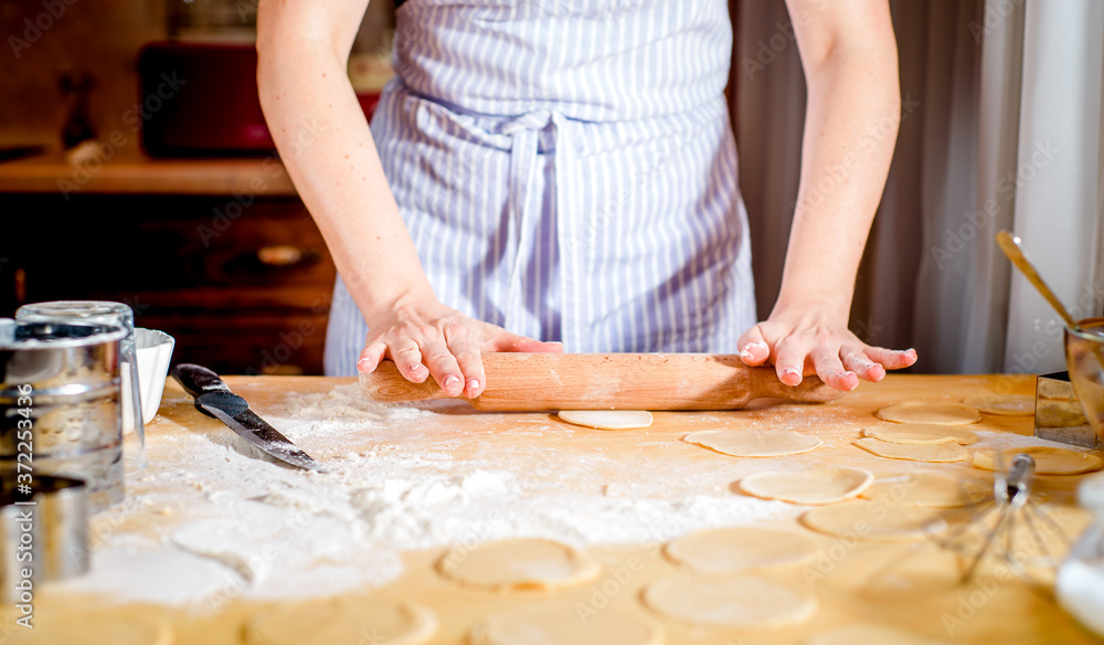 Female hands rolling out dough on kitchen table, close up Female hands rolling out dough on kitchen table, close up