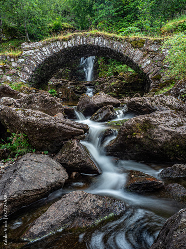 Canvas Print A packhorse bridge crossing a tributary below a waterfall on the south bank of the River Lyon