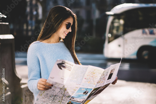 Charming young female tourist strolling during city tour  finding right direction enjoying spring weather, trendily dressed hipster girl sightseeing navigating using map with town routes on sunny day photo