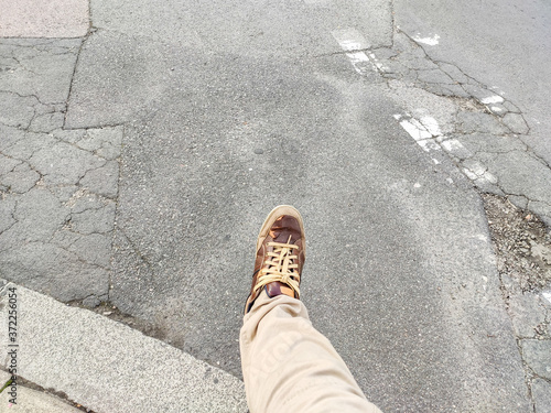 Man's leg and foot captured mid walking stride stepping out onto a cracked broken tarmac road photo