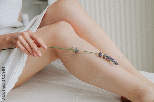 Model touching with lavender flower her legs. Pure leg skin concept. Wax Epilation concept. Sugaring concept.  photo