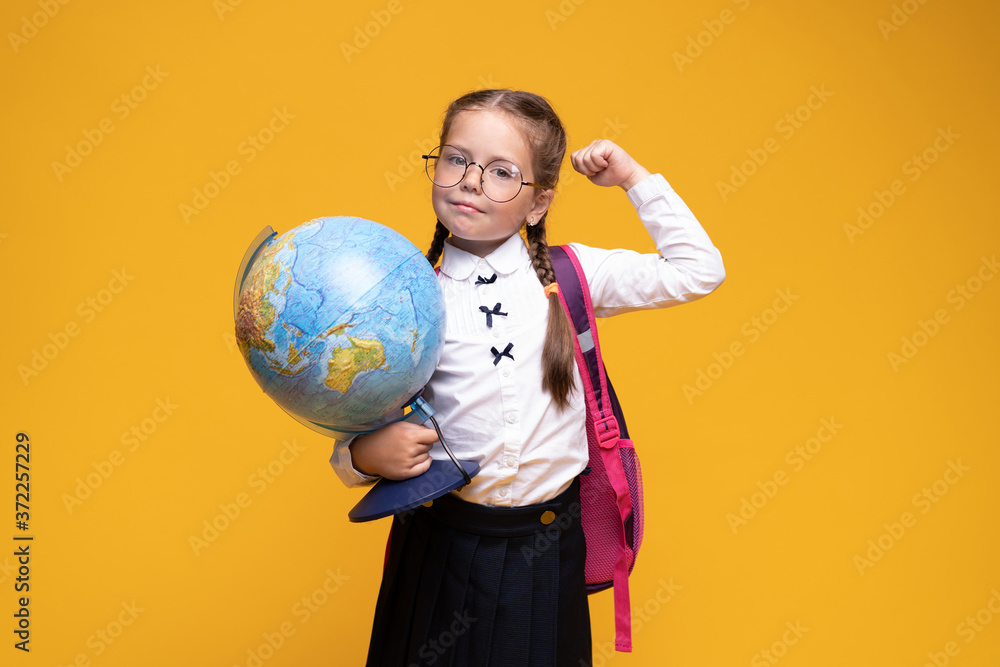 a little girl in school uniform holds a globe in her hands on a yellow background a little girl in school uniform holds a globe in her hands on a yellow background