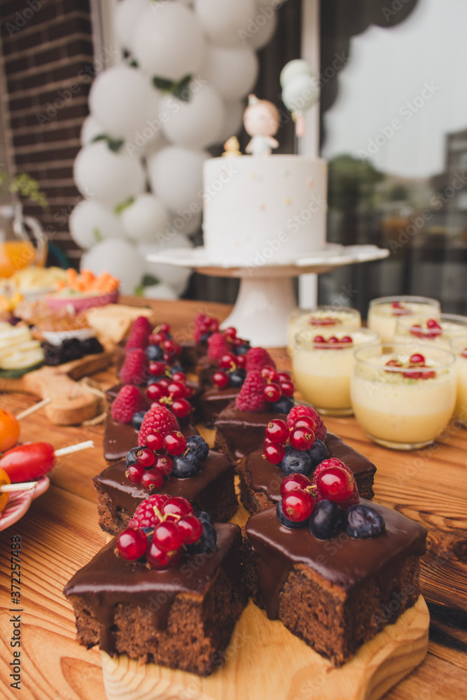 First anniversary party. Chocolate cake with berries on a wooden plate. Delicious desserts on rustic wooden table with the anniversary cake in the background. Diversity of pastry decorated with fruit.