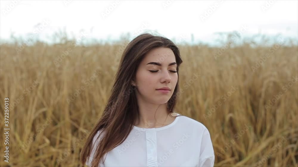 Attractive young girl in white clothes stands in the middle of a wheat field and meditates. Close-up. Slow motion Attractive young girl in white clothes stands in the middle of a wheat field and meditates. Close-up. Slow motion