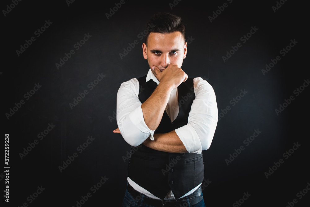 A handsome, young man, dressed in a white shirt and a cardigan from a suit on a dark background, is in a hurry or late, indicating the time, impatience, upset and angry for the delay. Time concept
