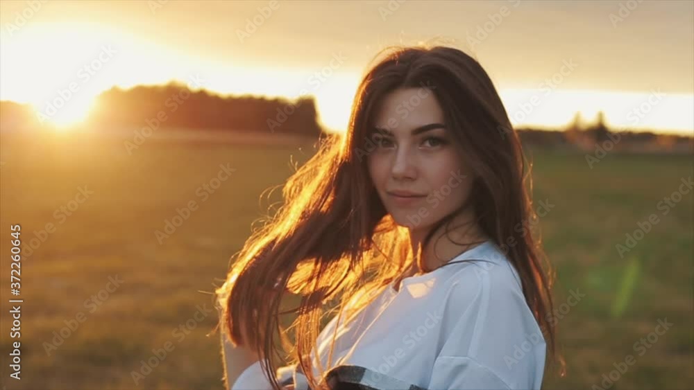 A sensual young girl is standing against the sunset and fingering her long hair with her hand. Close-up. Slow motion A sensual young girl is standing against the sunset and fingering her long hair with her hand. Close-up. Slow motion