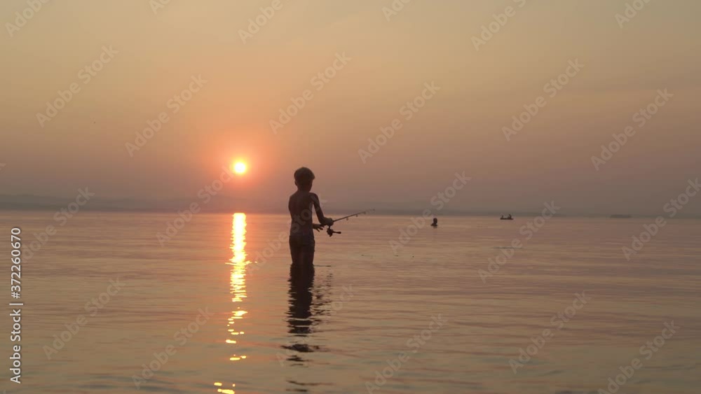boy fishing with a fishing rod standing in the water in the evening at sunset boy fishing with a fishing rod standing in the water in the evening at sunset