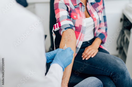 Nurse taking blood sample from young female patient in the background. Selective focus on sample tube.