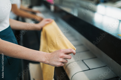 Young laundry worker pats the linen on the automatic machine at the dry cleaners.