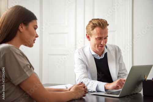 Cheerful cosmetologist pointing at laptop consulting young woman