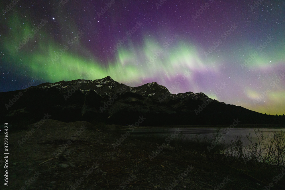 night dark sky with colourful aurora borealis dancing over a mountain