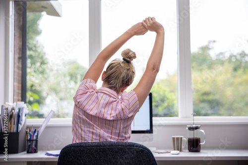 Rear View Of Woman Working From Home On Computer  In Home Office Stretching At Desk photo