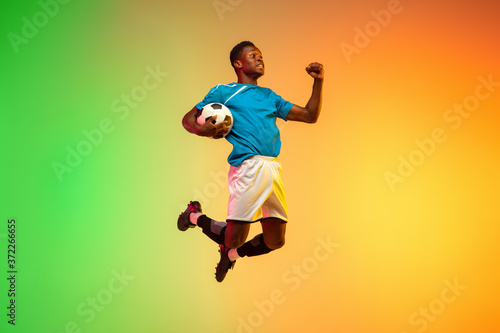 High jumping winner. Male soccer, football player training in action isolated on gradient studio background in neon light. Concept of motion, action, ahievements, healthy lifestyle. Youth culture. © master1305