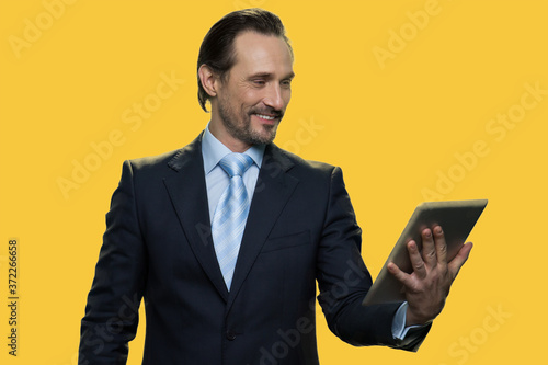 Happy businessman having video chat. Smiling caucasian man in business suit happily talking through digital tablet webcam on color background.
