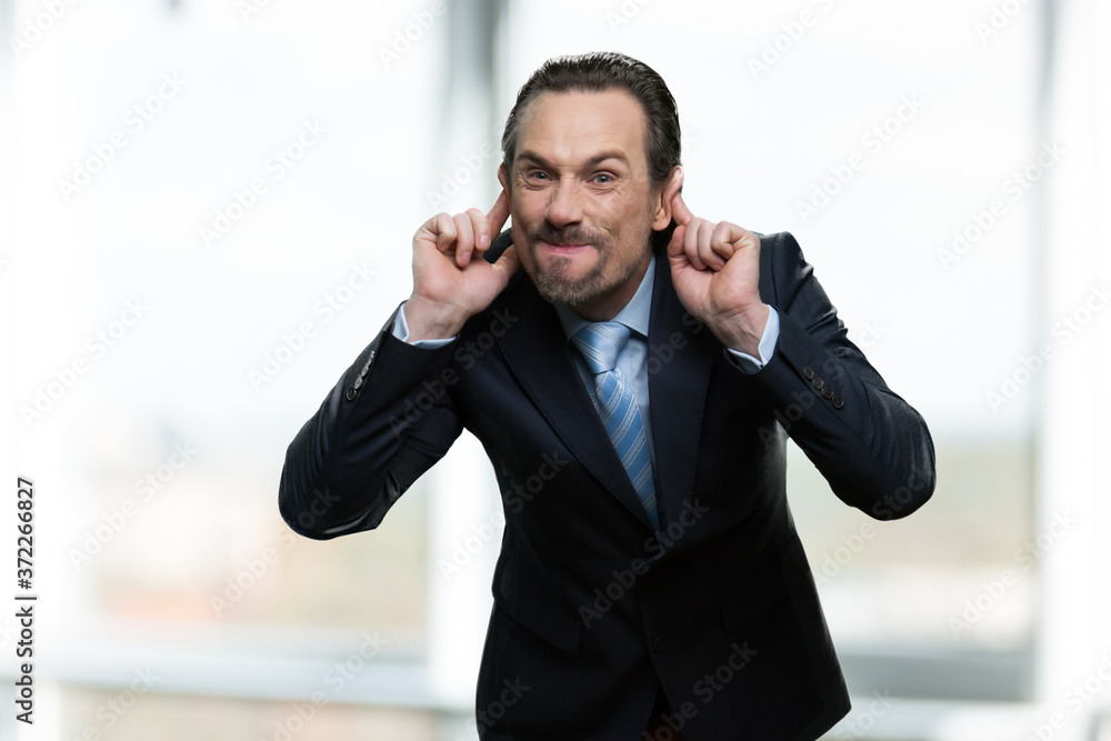 Mature businessman making monkey face. Caucasian man in business suit grimacing and teasing someone on blurred background. Mature businessman making monkey face. Caucasian man in business suit grimacing and teasing someone on blurred background.
