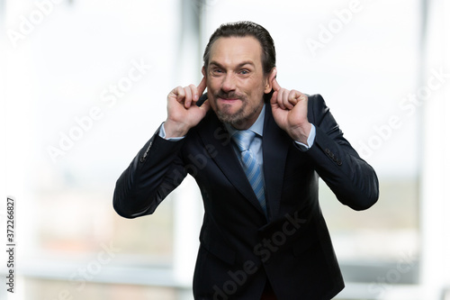 Mature businessman making monkey face. Caucasian man in business suit grimacing and teasing someone on blurred background.