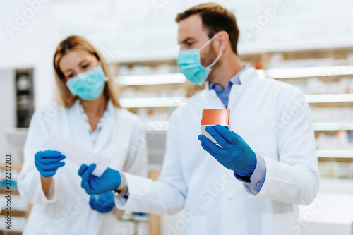Female and male pharmacists with protective mask on their faces working at pharmacy. Medical healthcare concept.