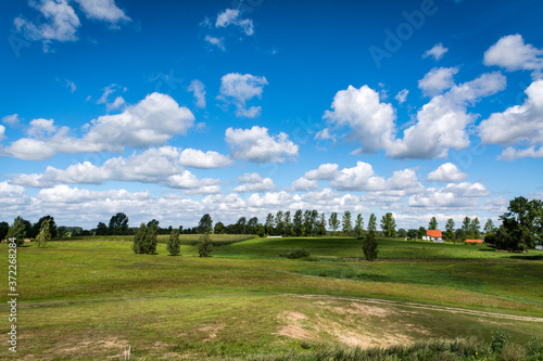 View from the top of a hill showing vast areas of meadows, forests, orchards, fields, and pasturelands connected together below a cloudy summer sky seen on a Polish countryside during a hike photo