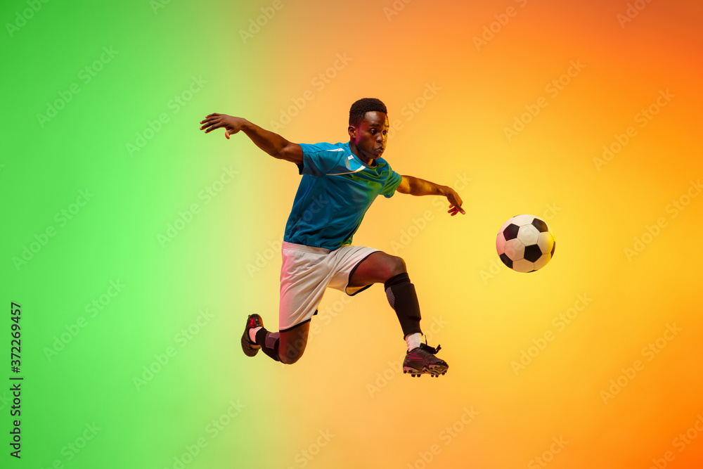 High jumping. Male soccer, football player training in action isolated on gradient studio background in neon light. Concept of motion, action, ahievements, healthy lifestyle. Youth culture.