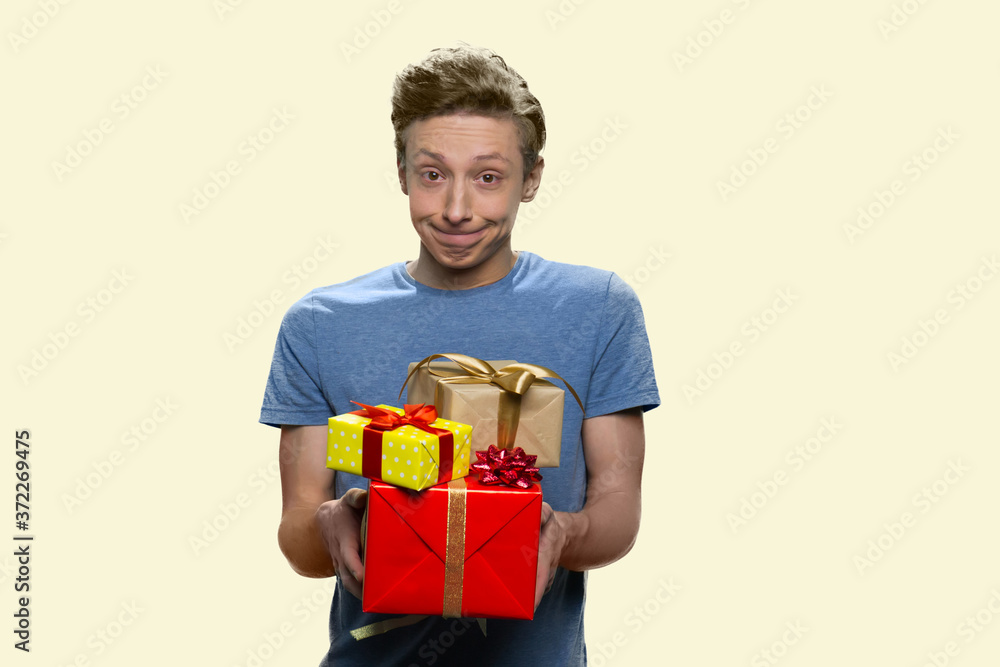 Funny teen boy offering gift boxes. Shy teenage guy holding stack of present boxes on white background. Happy holiday concept. Funny teen boy offering gift boxes. Shy teenage guy holding stack of present boxes on white background. Happy holiday concept.