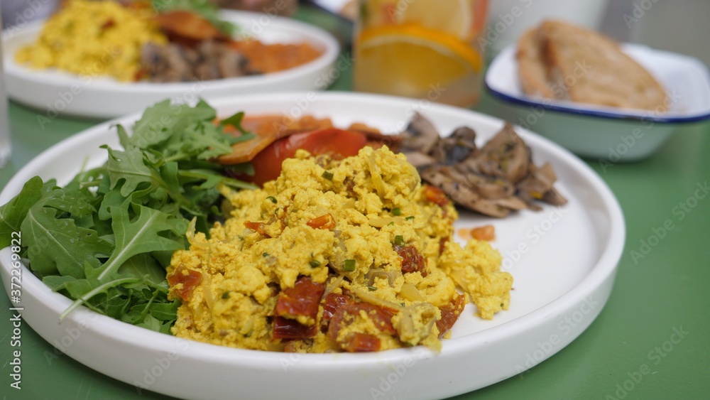 Vegan full English breakfast served on white plate in a cafe. Tofu scramble, beans vegan bacon. Healthy lifestyle concept