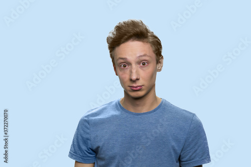 Teen boy looking at camera with surprise expression. Portrait of puzzled teenage guy standing with wide opened eyes against color background. photo