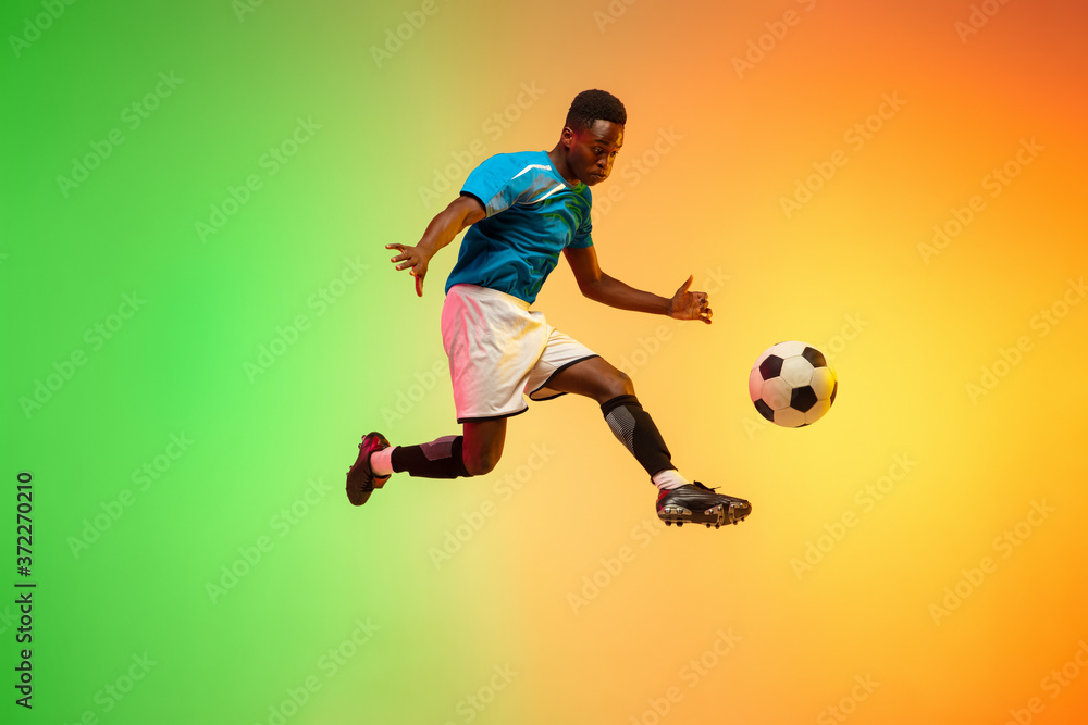 High jumping. Male soccer, football player training in action isolated on gradient studio background in neon light. Concept of motion, action, ahievements, healthy lifestyle. Youth culture.