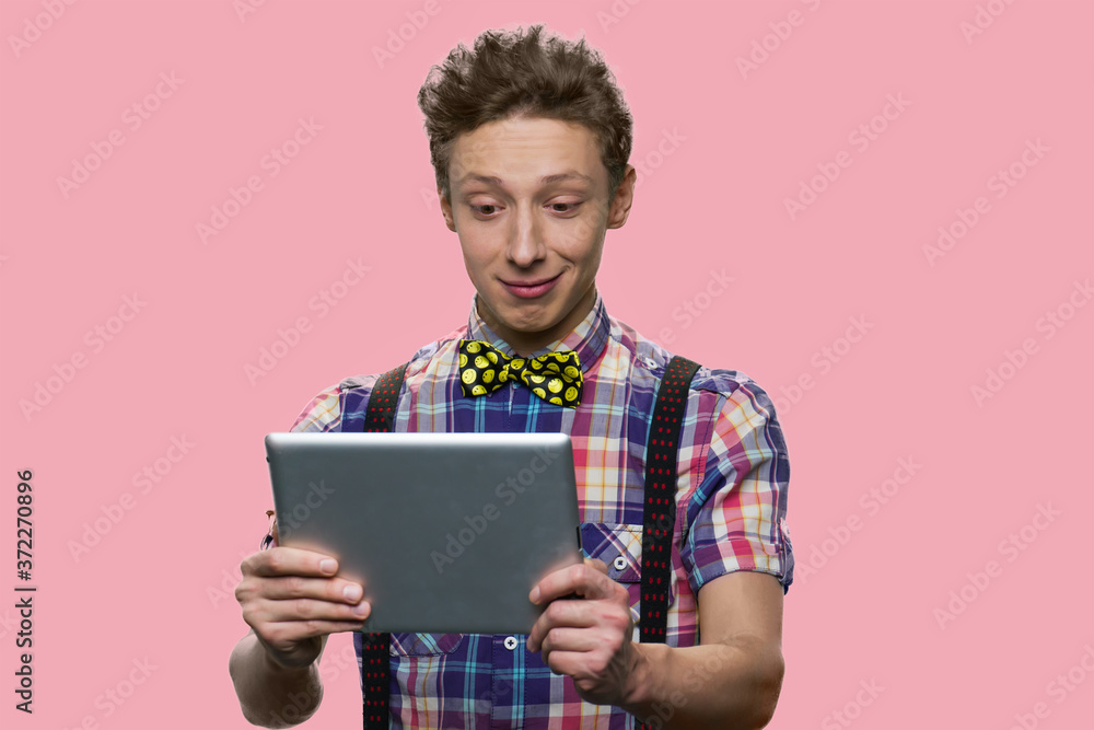Caucasian teenage boy looking at tablet pc. Cute teen guy having video chat using computer tablet against color background. Caucasian teenage boy looking at tablet pc. Cute teen guy having video chat using computer tablet against color background.
