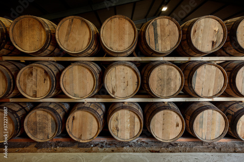 A front on view of a row of stacks of traditional full whisky barrels, set down to mature, in a large warehouse