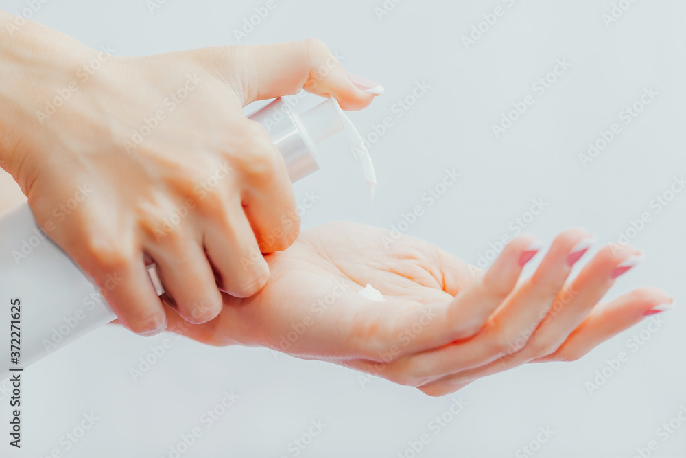 Woman applies cream to her hands from dispenser Woman applies cream to her hands from dispenser