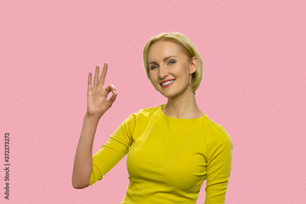 Beautiful woman showing okay sign with fingers. Charming blonde girl giving ok gesture and looking at camera on color background. Beautiful woman showing okay sign with fingers. Charming blonde girl giving ok gesture and looking at camera on color background.