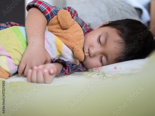 Asian child boy sleeping on bed in bed room. Young kid hugging favorite teddy bear and taking a nap for rest in day time.