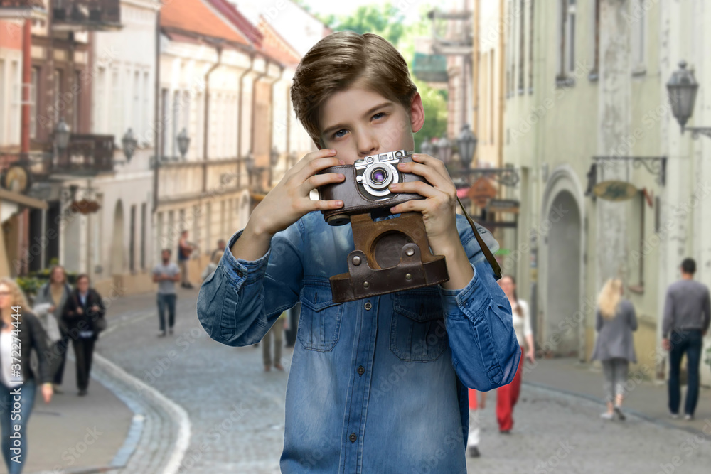 Little boy using vintage camera outdoor. Boy traveler in denim jacket taking picture with old retro camera. Tourism concept.