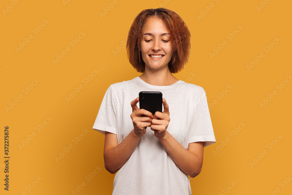 Young woman writes text messages on her mobile phone. Isolated on yellow background Young woman writes text messages on her mobile phone. Isolated on yellow background