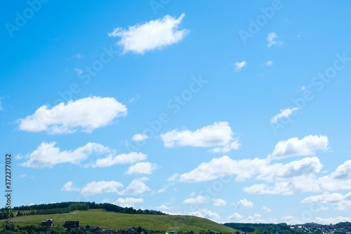 Blue summer sky with white clouds close-up and green hills. Rural landscape with trees on the horizon © Мария Мамонтова