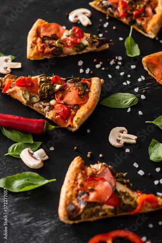selective focus of delicious Italian pizza slices with salami near vegetables on black background
