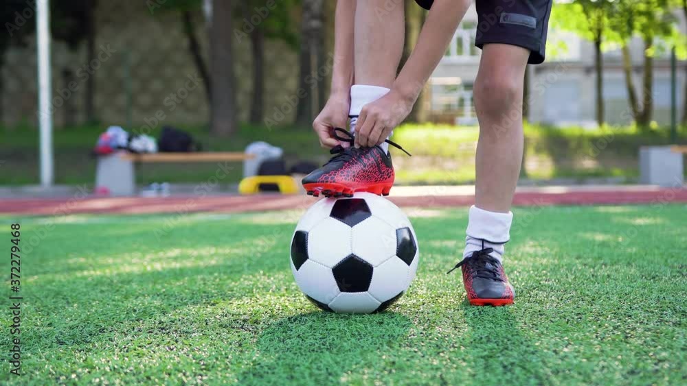 Portrait of teen boy which tying shoelace on his sport shoes during playing football on green field on training day,4k Portrait of teen boy which tying shoelace on his sport shoes during playing football on green field on training day,4k
