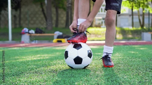 Portrait of teen boy which tying shoelace on his sport shoes during playing football on green field on training day,4k photo