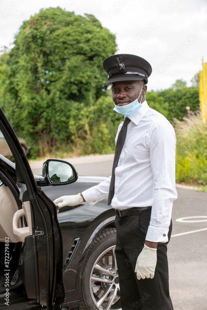 Hampshire, England, UK. 2020. A chauffeur entering his black car wearing a face mask and protective rubber gloves during the Covid-19 outbreak,