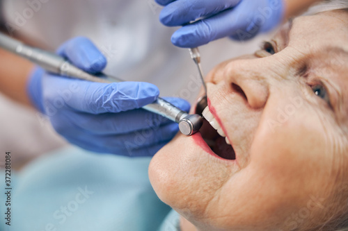 hands of doctor in blue gloves using drill while treating teeth
