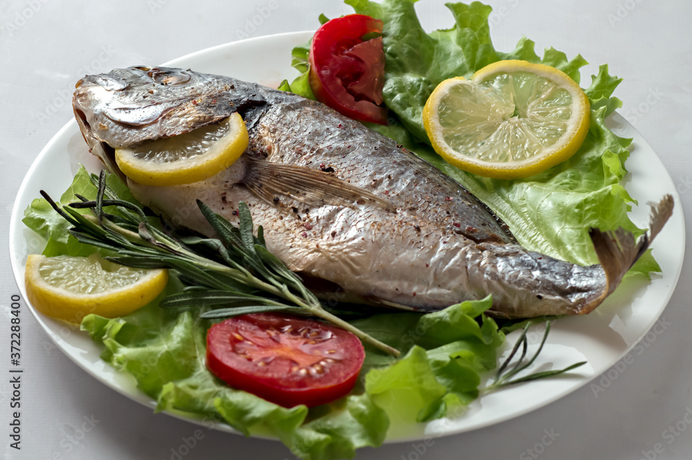 Baked dorado with vegetables, lemon, pepper, rosemary and lettuce. View from above.