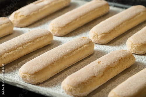 Ladies fingers cookies on a baking sheet with powdered sugar, savoiardi.
