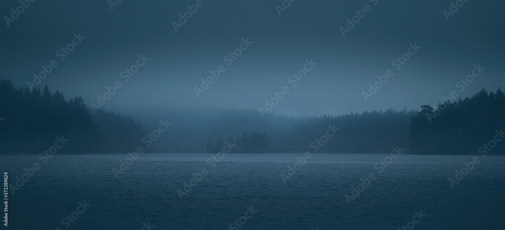 Fog over lake and forested islands. Blurred scenic view.