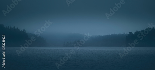 Fog over lake and forested islands. Blurred scenic view.